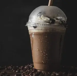 A vertical closeup of a plastic cup of cold coffee with a vanilla cream.